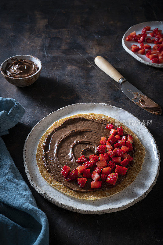 可丽饼Crêpes与可可奶油巧克力涂抹和草莓在黑木背景