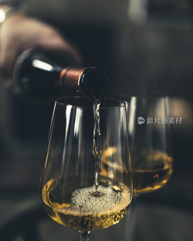 一个正在将白葡萄酒倒进玻璃杯的男人的手的特写。