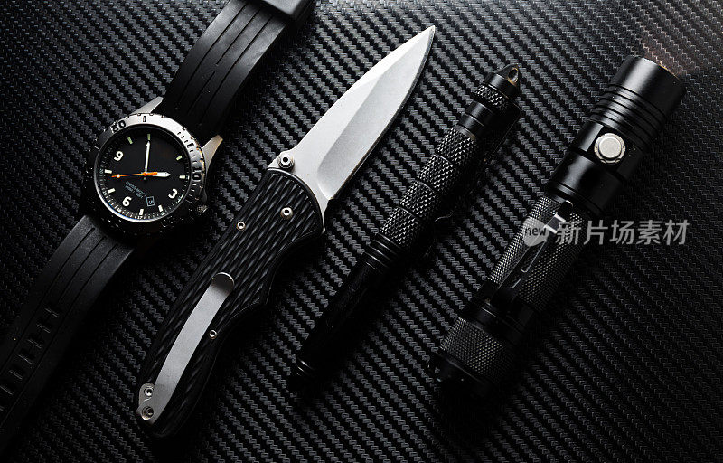 所有黑色战术EDC齿轮碳纤维背景(每天携带)与kubaton钢笔，折叠刀手电筒和手表