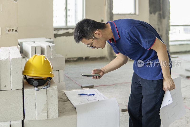 亚洲男性工程师，在装修工地处理建筑图纸和手机