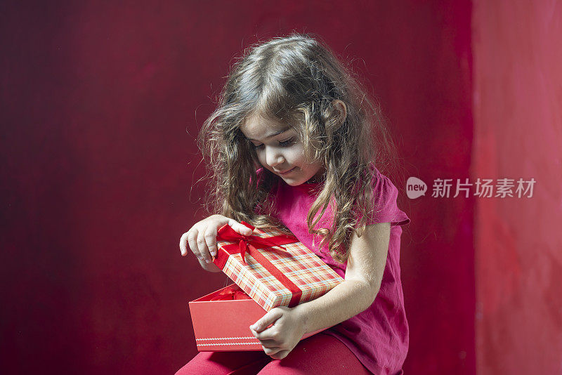 可爱的小女孩拿着红色背景的礼盒