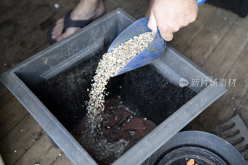 男性用铲子将砾石倒进一个方形的大花盆里