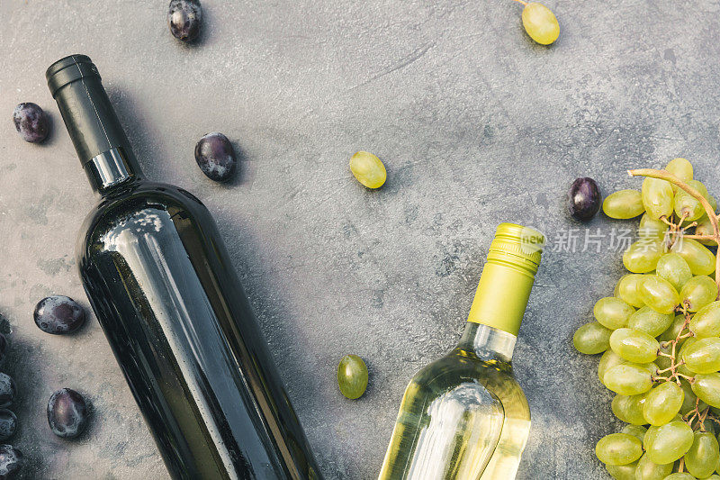 瓶身红色和白色的葡萄酒，绿色的藤蔓，葡萄酒杯和成熟的葡萄在古老的黑石桌背景。葡萄酒店、酒吧、酒庄或葡萄酒品尝概念
