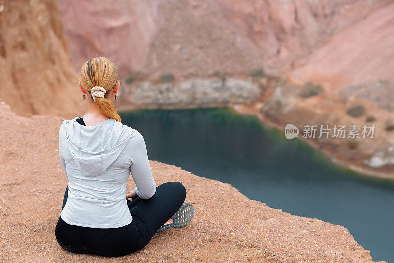 一名女子在狭窄的岩石之间的山湖前，以瑜伽姿势冥想