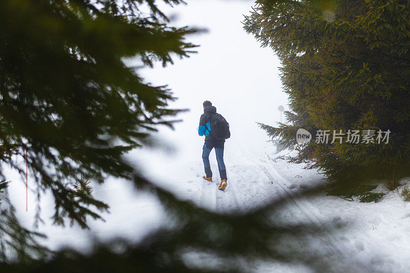 年轻的男性徒步旅行者穿着蓝色的夹克，在雾蒙蒙的雪山上走着，手里拿着地图