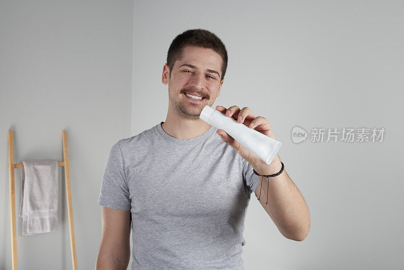 一个年轻人对着镜头微笑，展示着牙膏