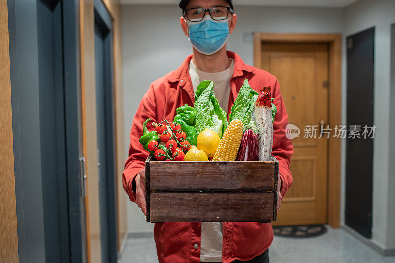 送餐员戴着防护口罩，手拿装有食物的纸袋在门口。快递员把装着新鲜蔬菜和水果的盒子交给顾客