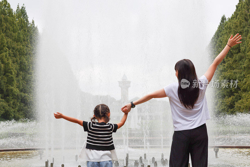 年轻的母亲和她的女儿在喷泉旁玩耍