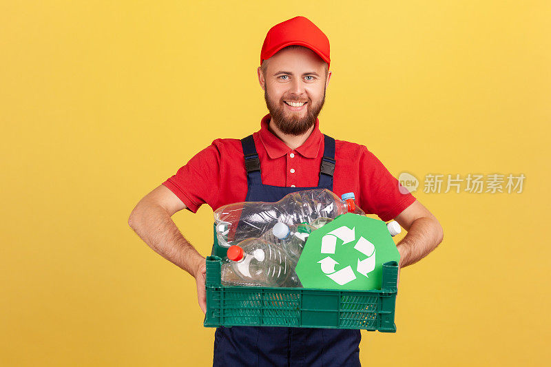 蓄着胡子的工人站着拿着塑料瓶和回收标志的箱子。