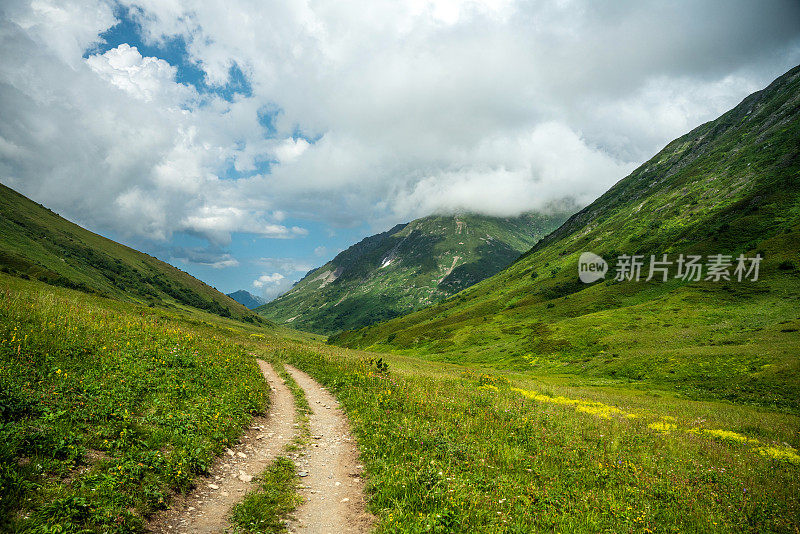 在阳光明媚的日子里，登山驿站在山上，美丽的群山四周被绿色的草和花覆盖着