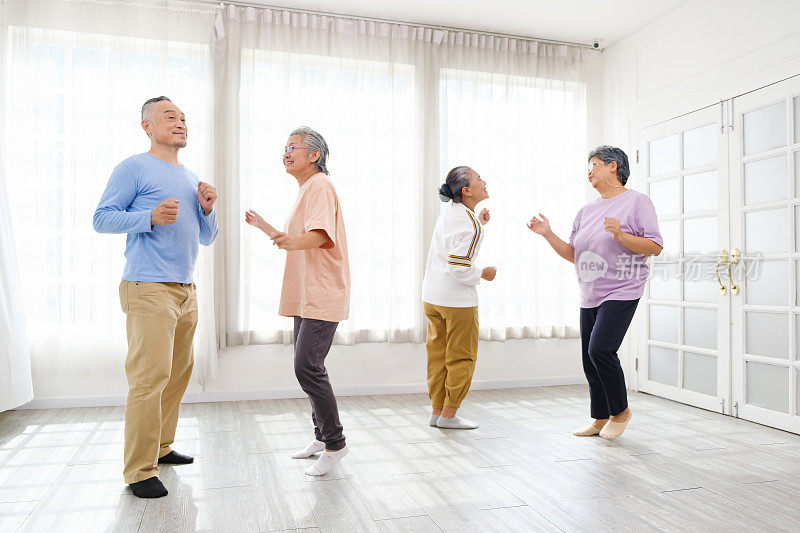 活跃的亚洲老年群体通过在家一起跳舞放松、微笑和大笑来混合男女锻炼。老年人和退休人员的室内活动。
