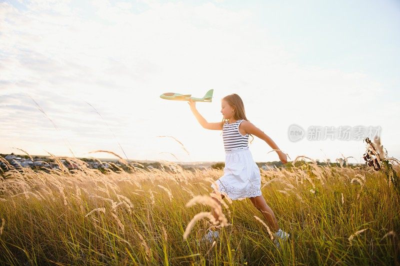 在落日的余晖中，快乐的女孩带着玩具飞机在田野上奔跑。孩子们玩玩具飞机。少年梦想着飞行，成为一名飞行员。女孩想成为一名飞行员和宇航员。缓慢的运动。