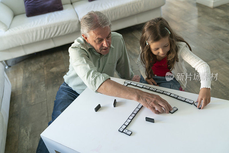 老人和孙女在家里客厅的桌子上愉快地玩多米诺骨牌