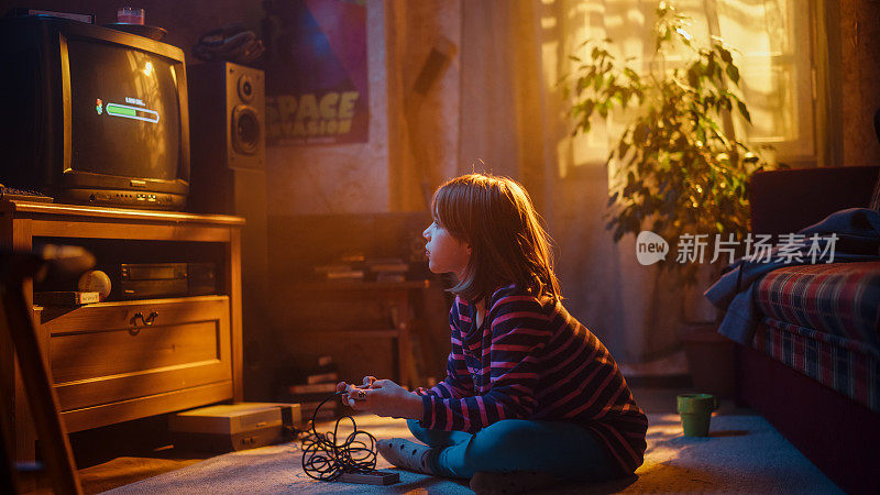 怀旧的童年概念:年轻的女孩在家里的复古电视机上玩老派街机视频游戏，房间内部的年代是正确的。孩子等待水平加载。