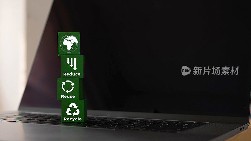 在笔记本电脑上放置有符号和文字的绿色木块减少了，重复使用和回收。减少电子垃圾，拯救世界，保护环境的理念。
