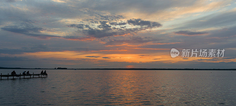 日落时分，一小群人坐在湖边的码头上，欣赏壮丽的云景