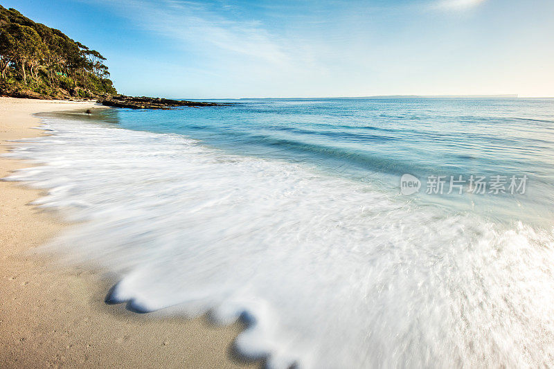 在晴朗蓝天的夏日里，波浪在白色沙滩上的潮汐模式