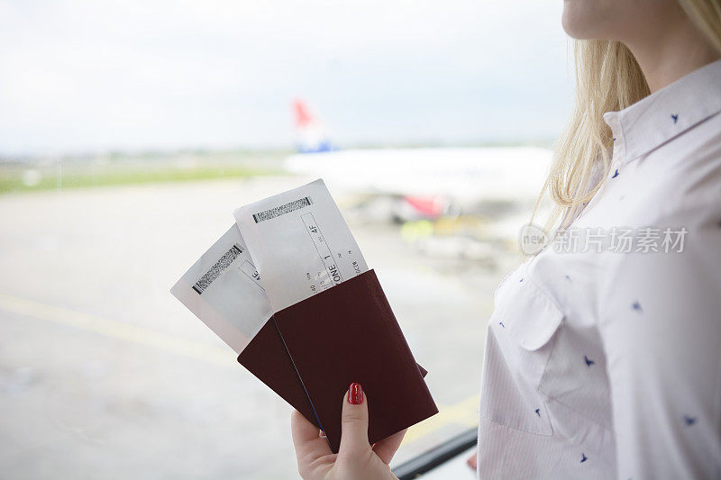 一位女士在机场拿着两本护照和两张机票
