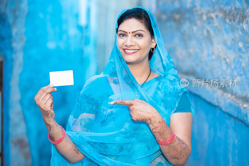 传统的印度妇女展示空白的信用卡借记卡模型，快乐的女性穿着纱丽指着空的商业或电子卡支付。