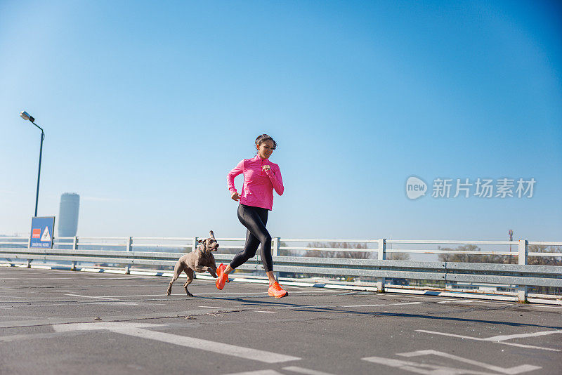 一个爱运动的女人带着她的狗在城市里空荡荡的停车场上跑步