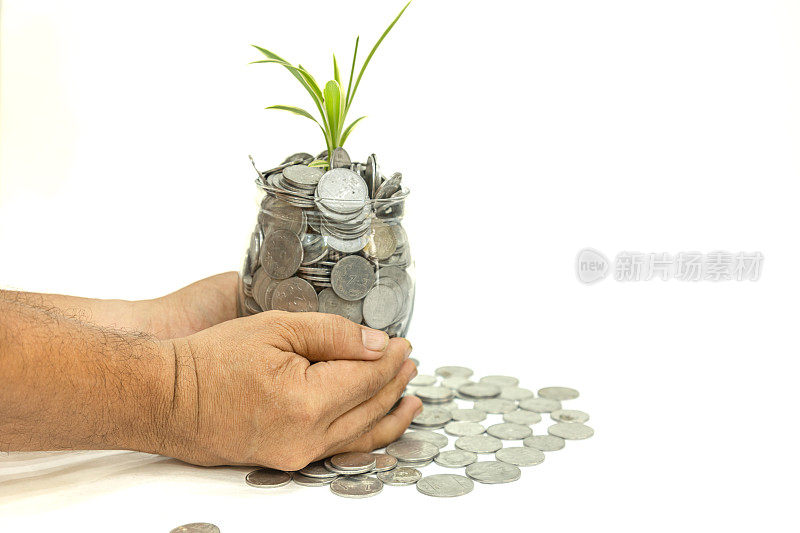 投资、利息和赚钱的观念。手里拿着一个装满硬币和正在生长的植物的玻璃罐