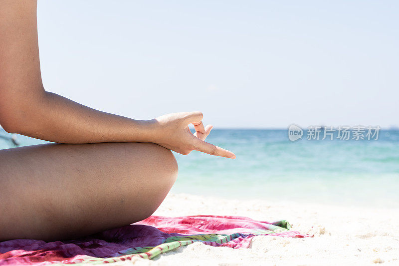 一个女人以莲花的姿势坐在沙滩上。她面朝大海，闭着眼睛。海滩是阳光明媚的，海洋是蓝色的。