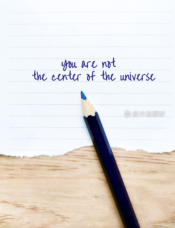用蓝色铅笔在便条纸上写着“你不是宇宙的中心”，认为一切都以自己为中心的人的观念，相信自己是每个人关注的中心。