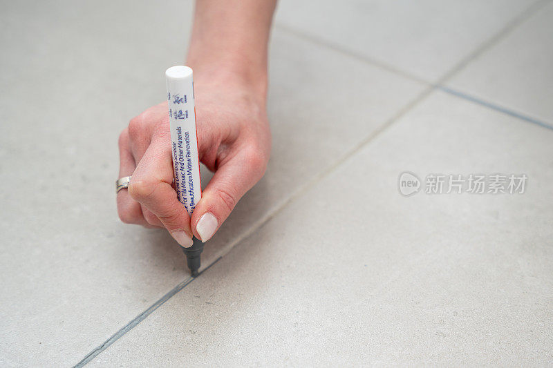 女性用灰色丙烯酸记号笔在地砖接缝处涂浆液，家装
