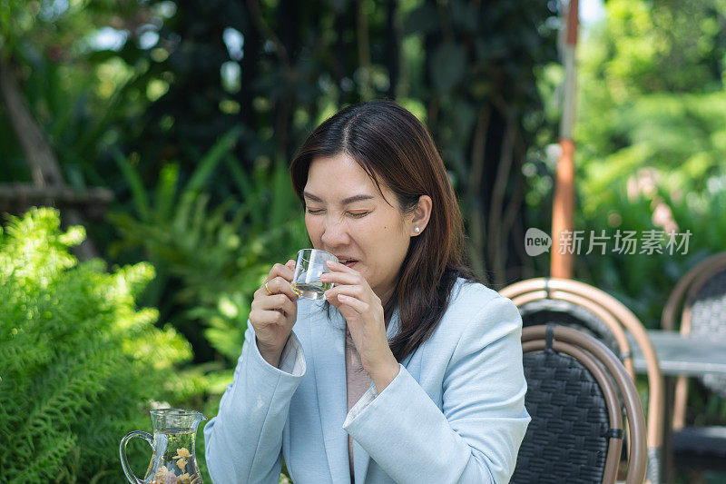 一名亚洲成年女性在户外咖啡馆喝着热茶，脸上带着悲伤的表情，感到牙痛。