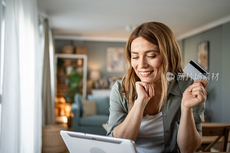 一位女士坐在房间里，用数码平板电脑和信用卡，通过网上银行查看每月的预算