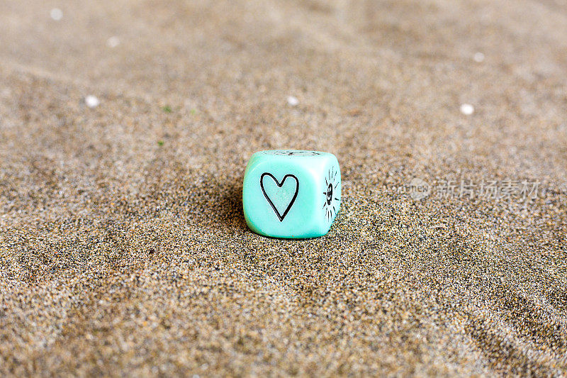 蓝色塑料立方体侧面的心形和太阳天气符号。沙子上有趣的赌博骰子。情人节的概念。爱的象征。带有复制空间的特写图片。柔情表达