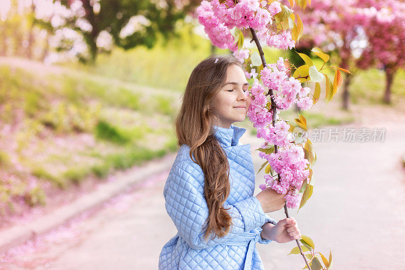 一个春天的少女的肖像，美丽的脸，眼睛在花园里的樱花树的特写。笑女赏樱。梦幻的女孩绽放着树枝上粉红色的花朵和自然的美丽。