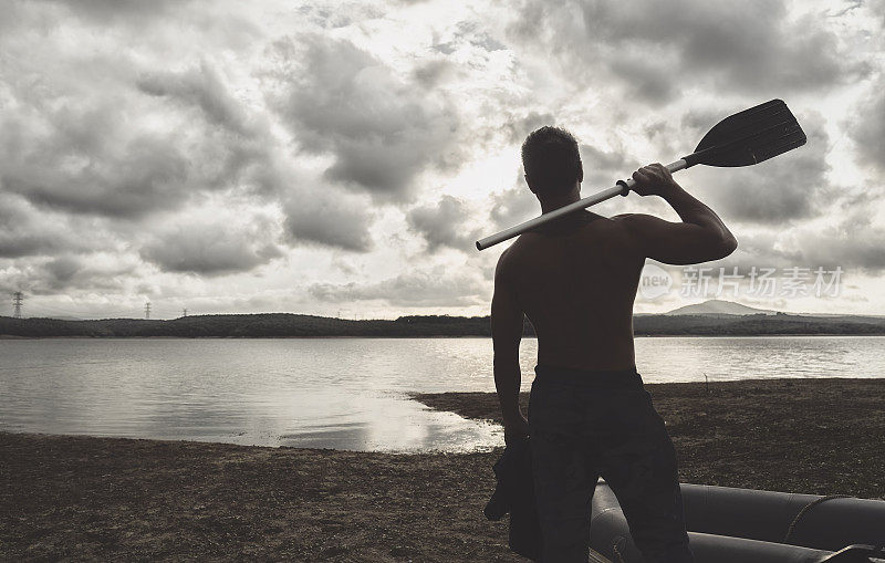 赤膊男子站在湖上，拿着独木舟划桨的日落