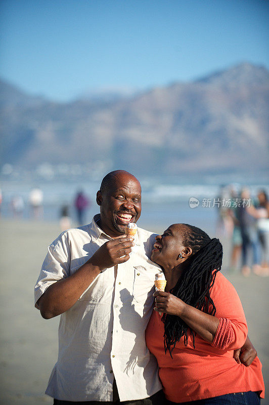活跃的老年夫妇在海滩上散步，一起吃冰淇淋