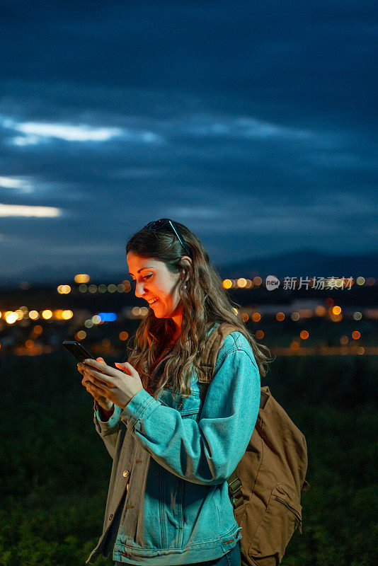 黄昏时分，一名年轻女子在城市附近使用手机