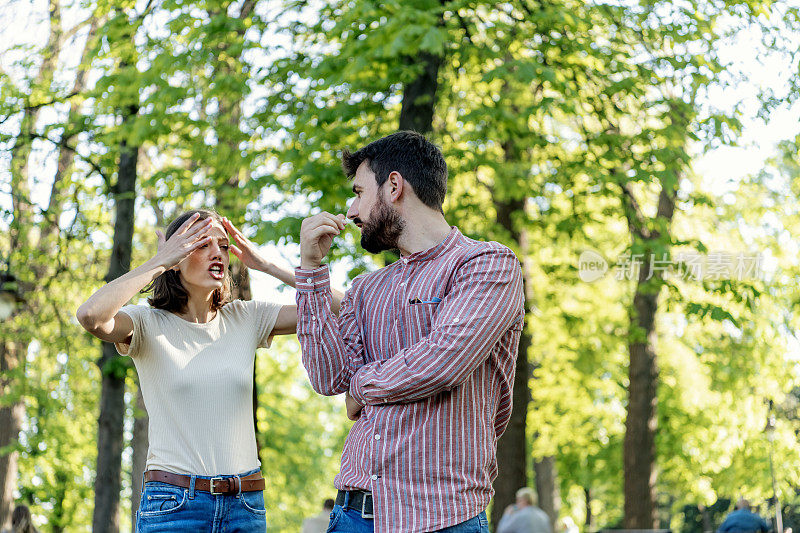 一对年轻夫妇在公园里吵架。年轻夫妇有一个夏天的一天争吵。站在公园外面，困惑的年轻女子打着手势，看着她的男朋友