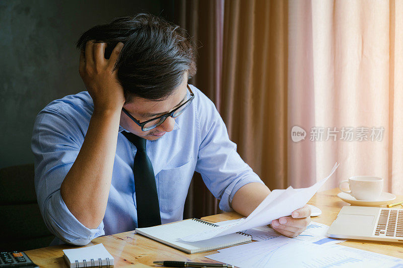 强调商人。一个年轻人坐在他的办公桌前，双手抱头，因为压力和总结报告。