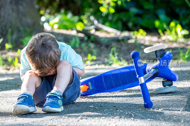三岁的小男孩从他的电动滑板车上摔下来后哭了