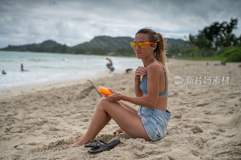 夏日――年轻女子在海滩上涂抹防晒霜，保护皮肤