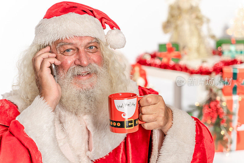 圣诞老人拿着手机，看着相机，喝着咖啡，茶，牛奶
