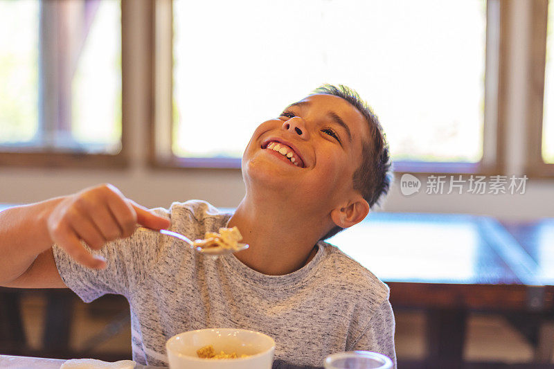 混合民族的小男孩吃早餐麦片和健康的水果和牛奶