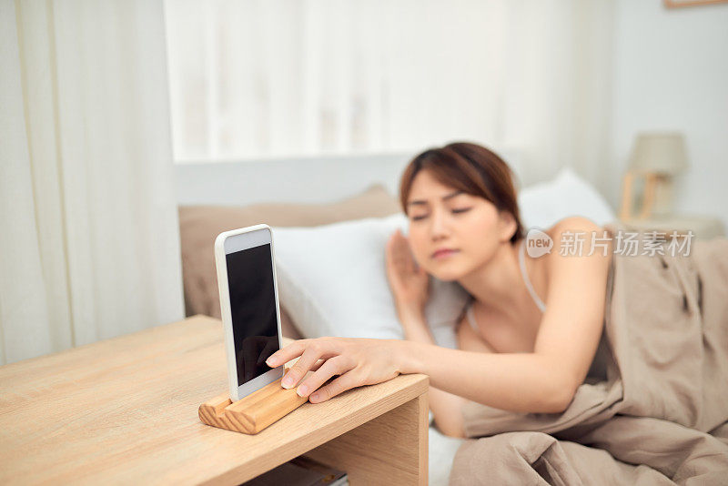 烦人的闹钟。女人躺在床上被手机吵醒，关掉了嘈杂的信号，特写