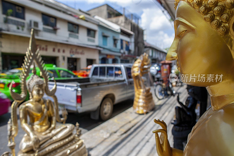 曼谷一家街头商店出售黄金佛像，背景是另一尊用塑料包裹的佛像，在一个繁忙街道的商店外出售。