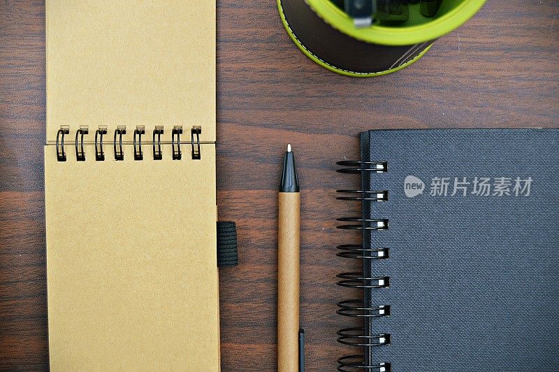 两个螺旋装订的记事本，一个打开，另一个用钢笔关闭，在一个棕色的桌面上