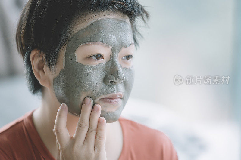 一位亚洲华人中年女性正在准备化妆，在家里脸部水疗，纵容自己的粘土面膜皮肤护理