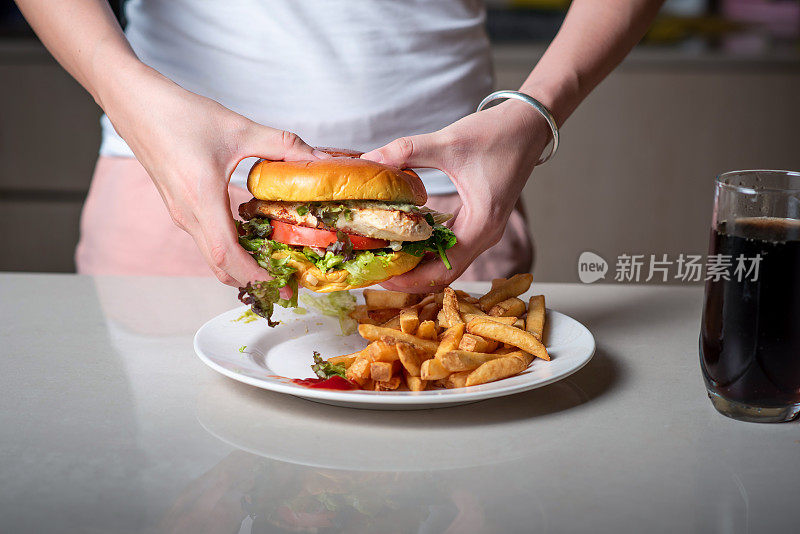 一个女人吃着盛在盘子里的鸡肉汉堡和炸薯条