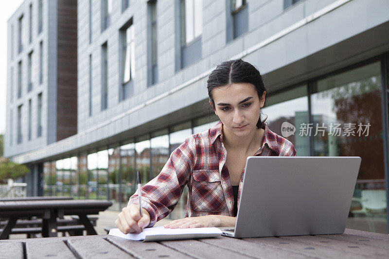 女大学生在校园里写作和使用笔记本电脑