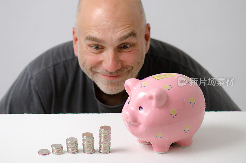 在粉色储蓄罐和一堆二角五分硬币后面微笑的男人