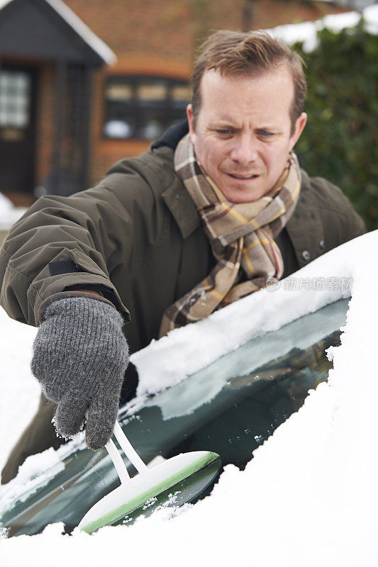 男人从汽车挡风玻璃上刮雪