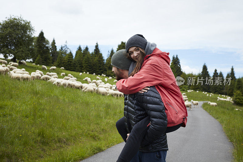 微笑的女人坐在男人的背上。羊吃草。山景观